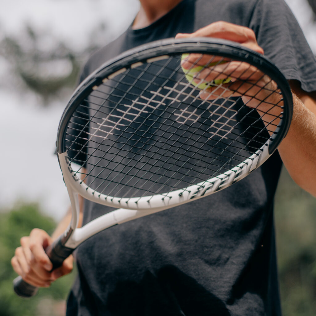 Tenniser met een groene tennisbal in een hand en een racket in zijn andere hand met een donker grijs shirt